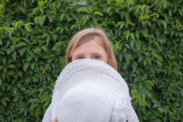 Portrait of a little girl in a white dress and with a hat on a green grape leaf background