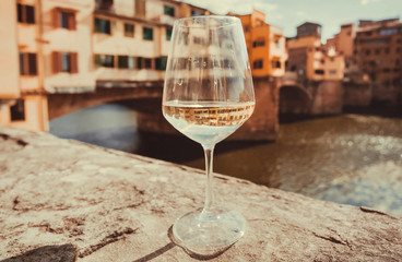 Obraz na płótnie Canvas Wine glass and view on bridge Ponte Vecchio in historical Florence, Tuscany. River and ancient cityscape in Italy