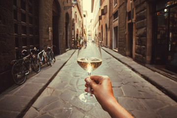 Wine glass in hand of happy tourist walking past historical houses of Florence, Tuscany. Ancient streets in Italy