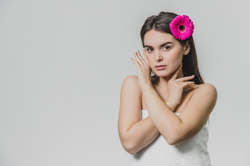 Beautiful young girl standing on a white background. During this time there is a flower in the hair. During this hand on the arm on the chest. Has beautiful black long hair.