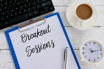 Top view of keyboard,coffee,clock,pen,clipboard and paper written with Breakout Sessions.