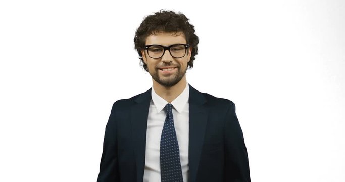 Good looking smiled man in glasses, suit and tie doing ok gesture with fingers while standing on the white screen background.