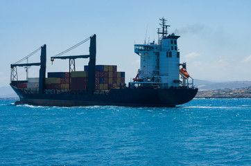 Container ship sails out of the Bay of Heraklion in the open sea in the background of the mountains and the port
