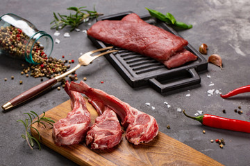 Set of Raw uncooked black angus beef tomahawk steaks on bones and veal tenderloin served with chilli and peppercorns. Rustic style.