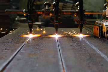The machine cuts metal sheets with gas. Flying spray molten metal. Side view. three gas cutter...