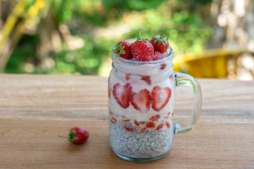 Almond milk chia pudding with fresh red strawberries, goji berries and oat flakes in a glass jar mug. Vegan raw breakfast. Chia seeds and fresh cut fruits and berries dessert