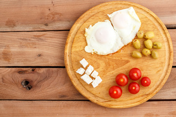 Breakfast. Fried eggs, tomatoes, olives and cheese on a wooden plate. Top view