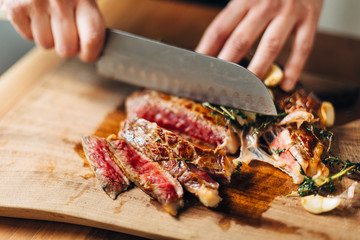 Chef slicing ribeye steak on a wooden board