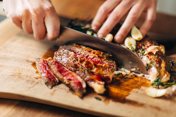 Chef slicing ribeye steak on a wooden board