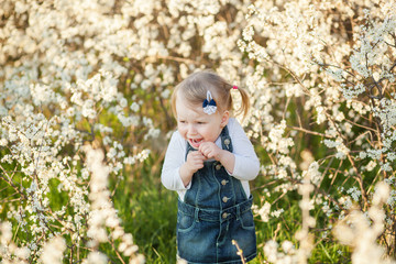 Closeup portrait of a happy little blond girl 2-3 years old in white shrub colors in a park. Different emotions on her face. Free space for text, copy space.