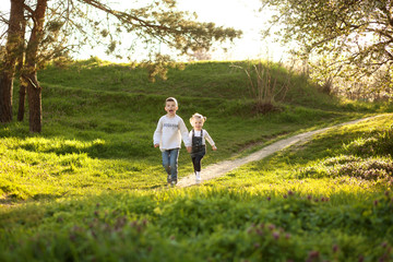 Naklejka premium Cute children boy and girl friends running through the park in spring on a sunny day.