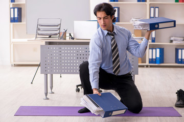 Young handsome male employee doing exercises in the office 