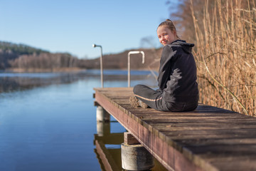 junges M&auml;dchen /  Teenager sitzt im Sonnenschein auf einem Badesteg