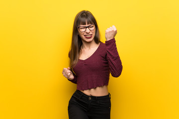 Woman with glasses over yellow wall celebrating a victory
