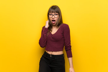 Woman with glasses over yellow wall with surprise and shocked facial expression