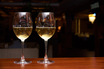 Two glasses of white wine with a reflection on the bar.