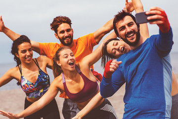 Group of young sports people doing seflie on the beach by the sea