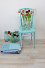vintage turquoise chair with pink tulips in glass vases and a folded quilt