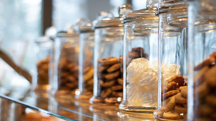 Many glass jars with caps filled with cookies and sweets, on defocused background with reflection. Jars contain marsh-mallow and cookies. Background for cafeteria or restaurant. Horizontal banner