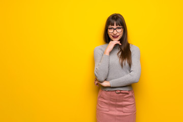 Woman with glasses over yellow wall smiling