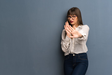 Woman with glasses over blue wall is a little bit nervous and scared stretching hands to the front