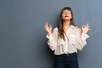 Woman with glasses over blue wall in zen pose