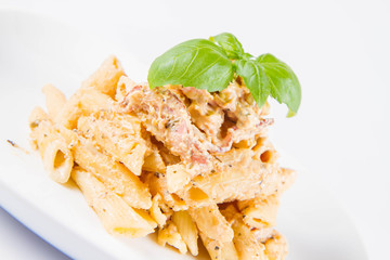 Pasta - penne with white cream sauce with bacon on a plate, decorated with fresh basil	