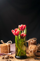 Simple rustic still life of red tulips in a green glass and stacks various cookies on wooden table.