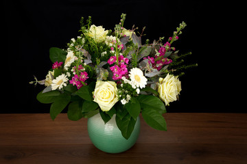 Bouquet with a variety of multicolored flowers in a rustic vase on wooden background