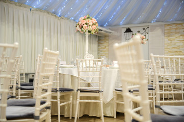wedding table setting in a banquet hall in white color: a round table with flower arrangement on it surrounded by chairs