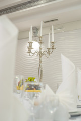 close up photo of a silver candlestick with white candles on a table in a banquet hall