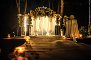 wedding arch decorated with flower compositions and curtains at night; a path with candles that...