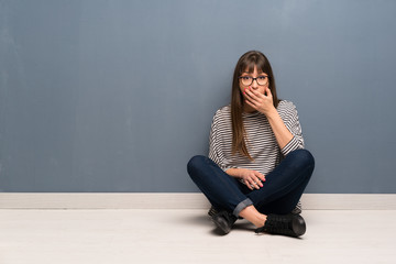 Woman with glasses sitting on the floor surprised and shocked while looking right