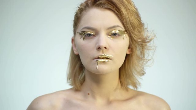 High Fashion model woman in golden make up posing in studio. Portrait of beautiful sexy girl, trendy glowing gold skin make-up. Art design make up. Girl with gold makeup.