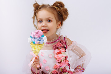 little girl in a pink dress with flowers holding a candy on a stick, licking, sweets in childhood. sweet life.