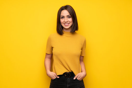 Young woman over yellow wall laughing looking to the front