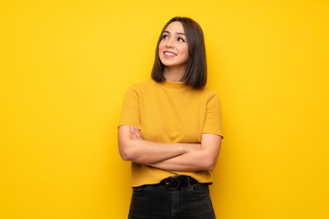 Young woman over yellow wall looking up while smiling