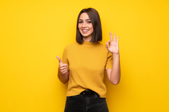 Young woman over yellow wall showing ok sign with and giving a thumb up gesture