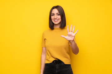 Young woman over yellow wall counting five with fingers