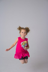 little girl in a coral dress holding a candy and jumping, in a jump. fun, sweet baby life, carelessness