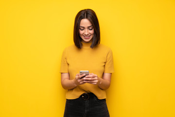 Young woman over yellow wall sending a message with the mobile