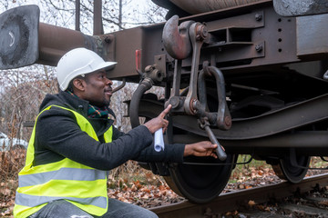 Afro-American train mechanic wearing safety equipment (helmet and jacket) checking and inspecting...
