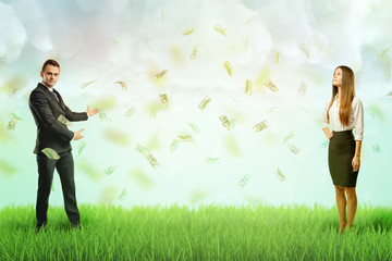 Businessman and businesswoman standing each at different side of green lawn with rain of dollar bills in the air.