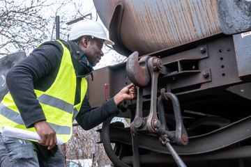 Afro-American train mechanic wearing safety equipment (helmet and jacket) checking and inspecting gear train