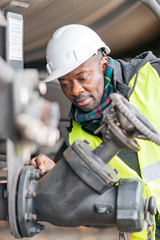 Afro-American train mechanic wearing safety equipment (helmet and jacket) checking and inspecting gear train