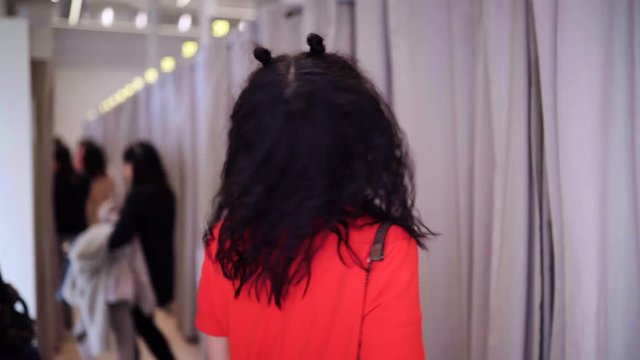 Sensual girl trying on a red long jacket  in a fitting room in clothing store and admiring of herself In mirror, touching her body.