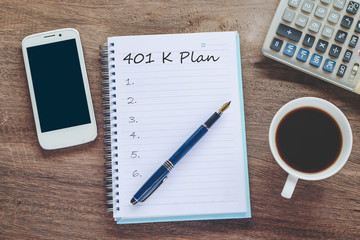 401K Plan text on book note with cup of coffee, pen and smartphone.