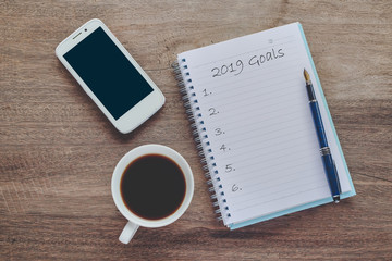 2019 goals text on book note with cup of coffee, pen and smartphone.