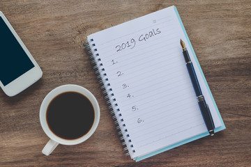 2019 goals text on book note with cup of coffee, pen and smartphone.
