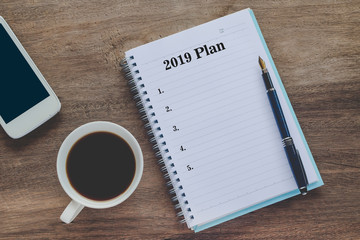 2019 Plan text on book note with cup of coffee, pen and smartphone.